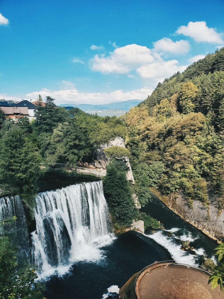 waterfalls near green trees under blue sky during daytime